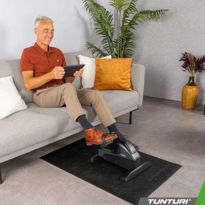 Mann tritt auf dem Sofa sitzend in die Pedale des Tunturi Mini Bike